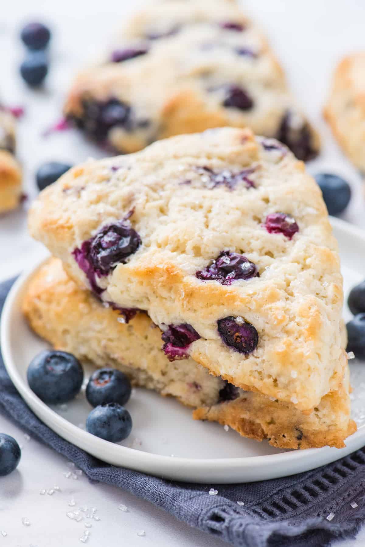 two blueberry scones stacked on each other on white plate with blue napkin