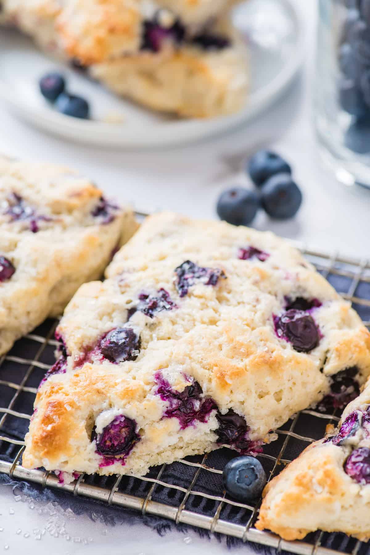 blueberry scones on wire cooling rack with blue napkin underneath on white background