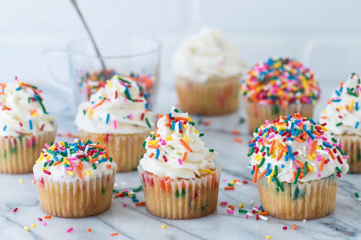 3 funfetti cupcakes with white frosting topped with rainbow sprinkles