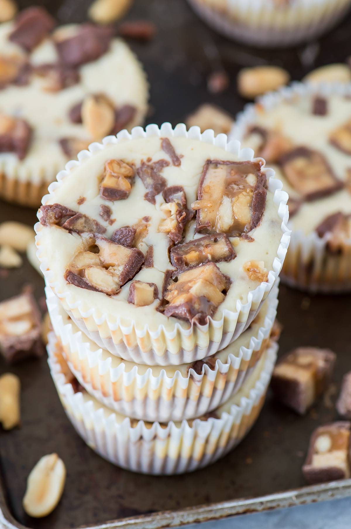 mini snicker’s cheesecakes stacked 3 high on a dark metal baking sheet