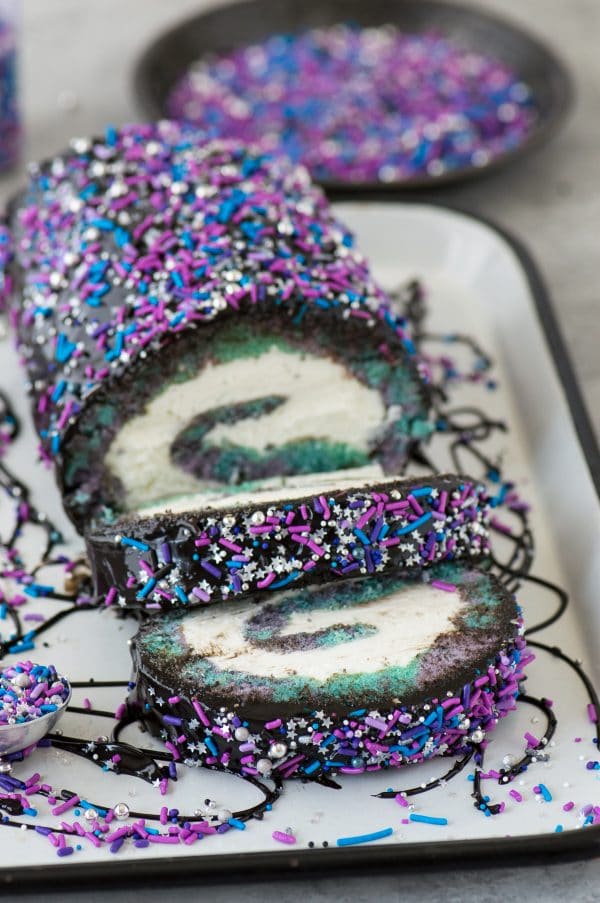 Multi-colored galaxy cake roll with black chocolate ganache, topped with sprinkles!