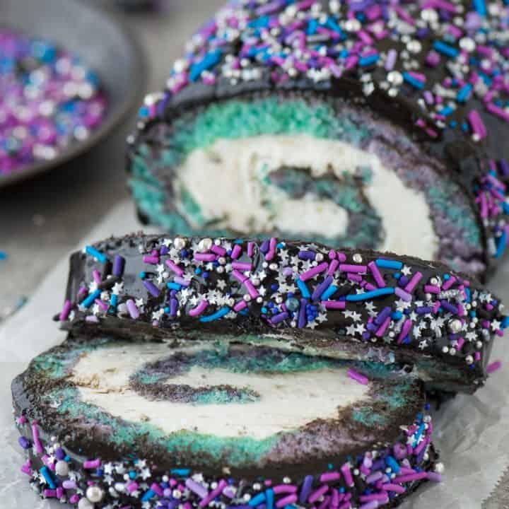 Multi-colored galaxy cake roll with black chocolate ganache, topped with sprinkles!