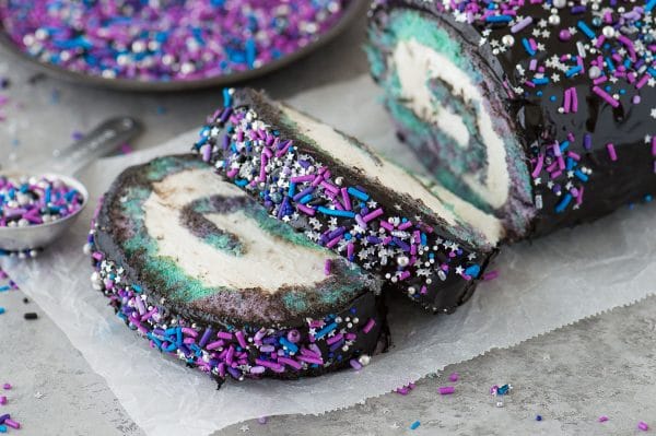 Multi-colored galaxy cake roll with black chocolate ganache, topped with sprinkles!