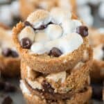Three stacked 5 ingredient indoor S’mores Cups surrounded by other delicious s'mores cups on a baking dish.