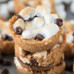 Three stacked 5 ingredient indoor S’mores Cups surrounded by other delicious s'mores cups on a baking dish.