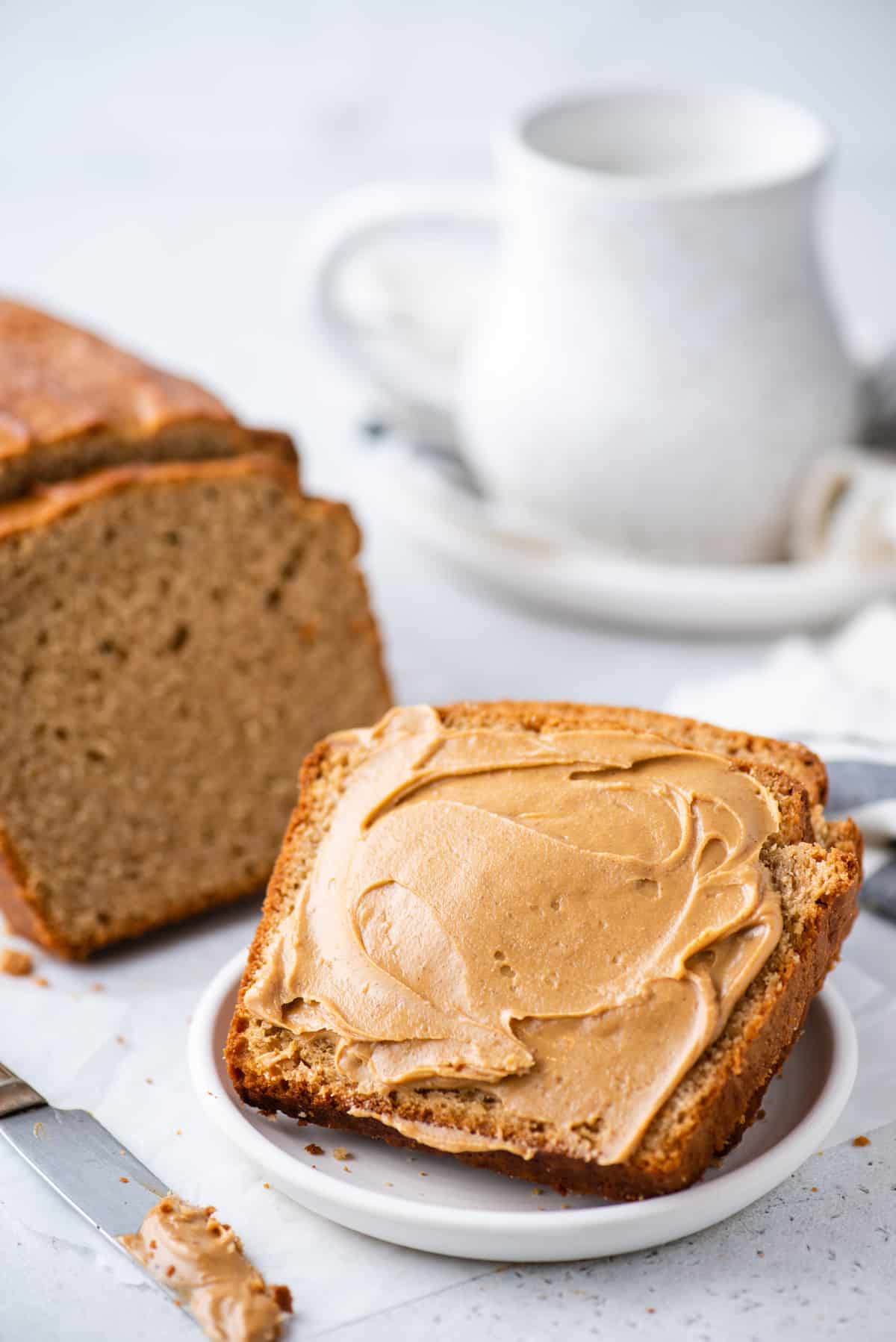 slice of peanut butter bread with peanut butter on white plate on white background