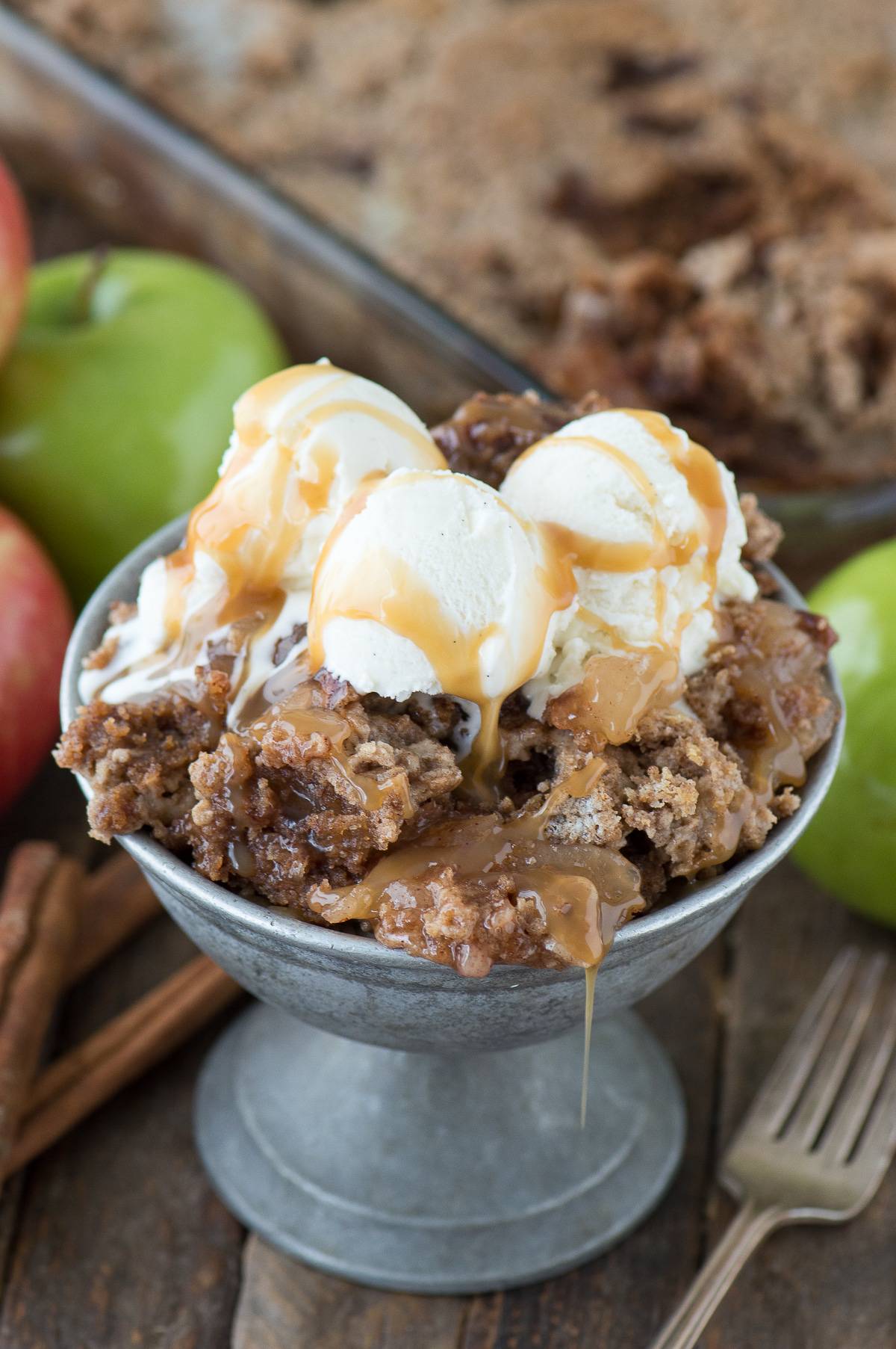 apple dump cake with 3 ice cream scoops and caramel sauce in metal bowl