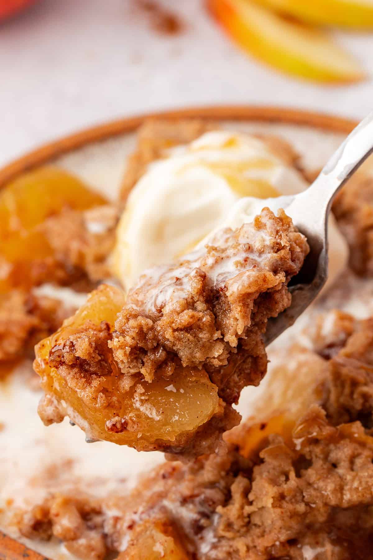 A close-up of a fork holding a bite of apple dump cake with tender apples and crumbly topping. A scoop of melting vanilla ice cream mingles with the dessert on a ceramic plate, creating an irresistible blend.