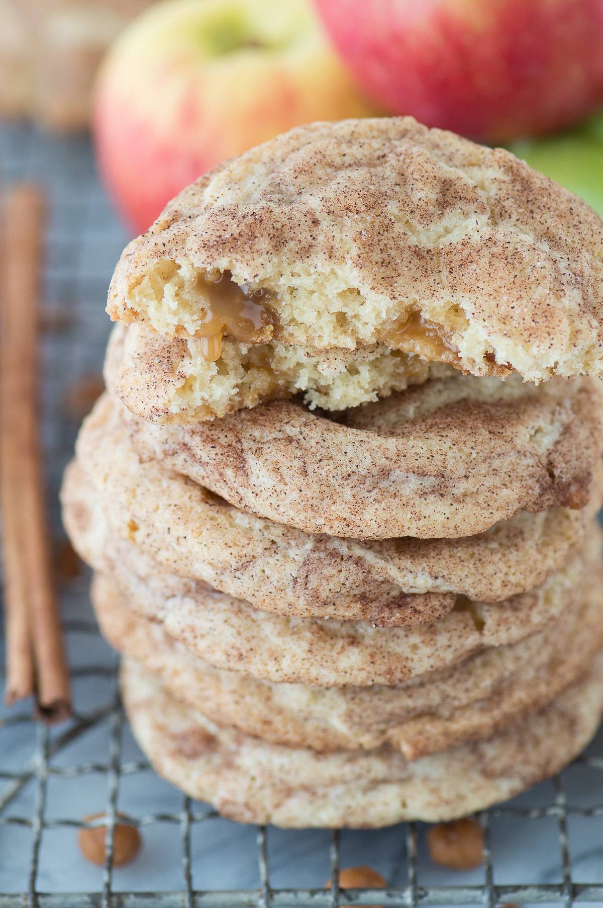 caramel apple snickerdoodle cookies stacked on top of each other on a metal cooking rack with apples in background