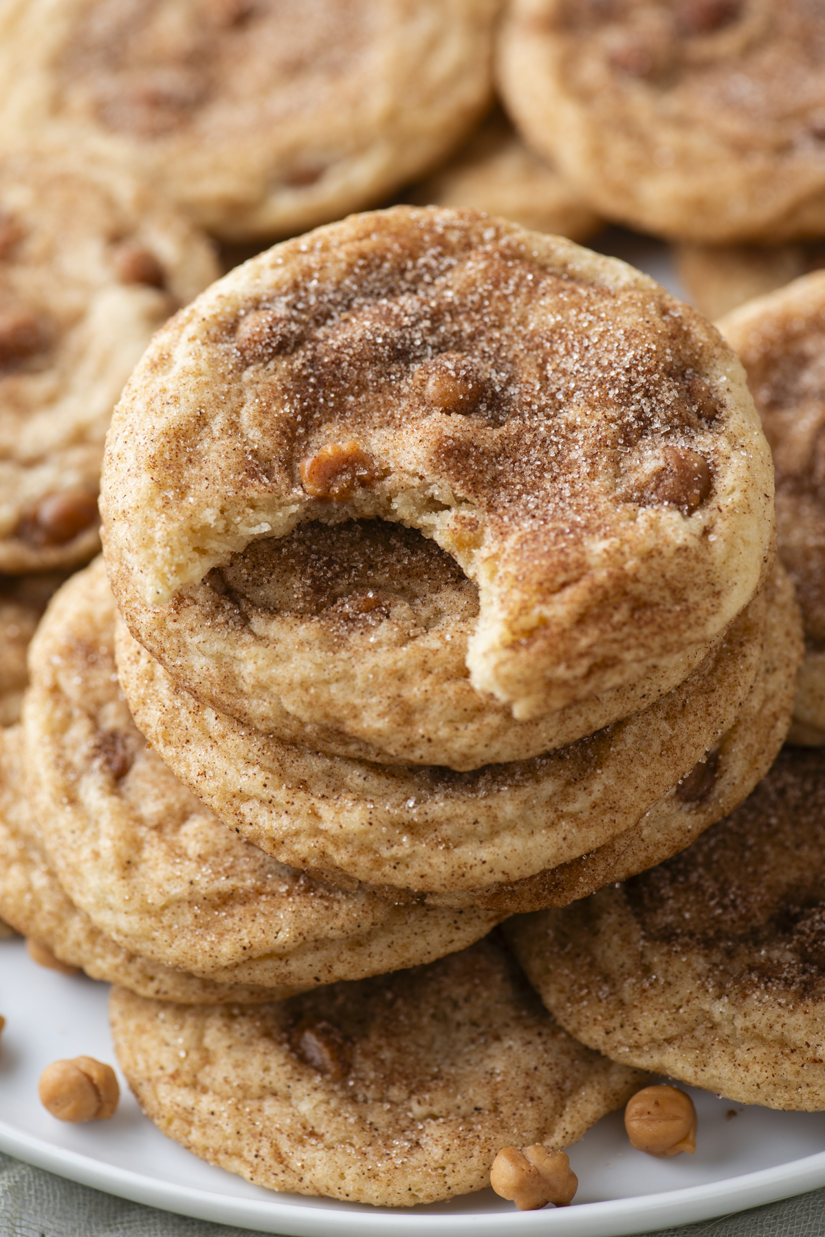 A stack of cinnamon sugar cookies with butterscotch chips is shown, reminiscent of caramel apple snickerdoodles, with the top cookie missing a bite.