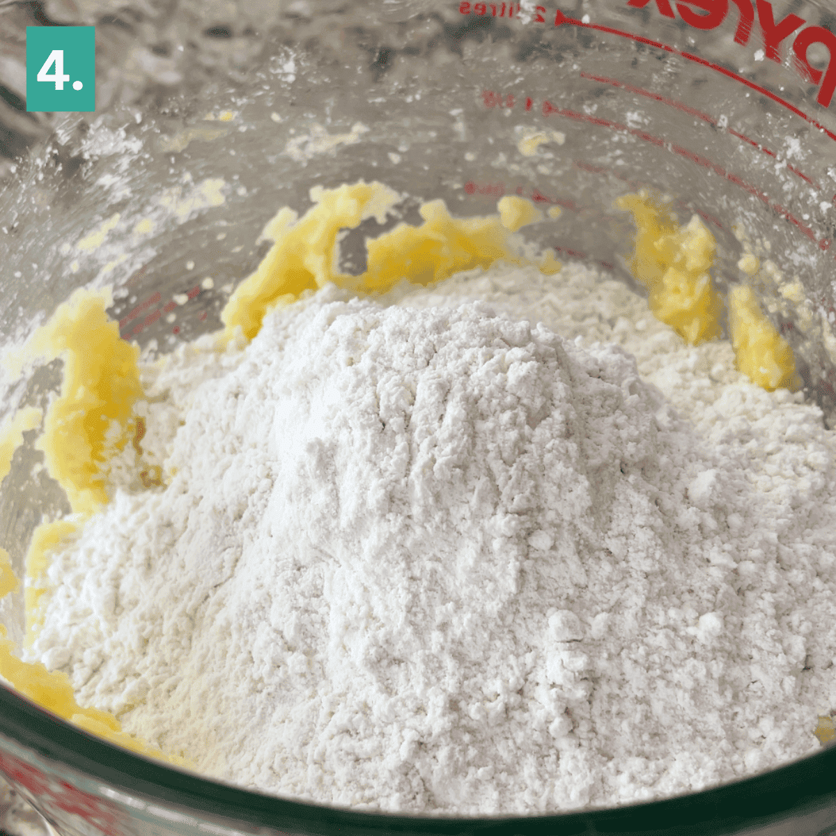 A glass mixing bowl holds creamed butter and a mound of flour, ready to become delicious caramel apple snickerdoodles. The bowl has red measurement markings, and a green square with the number 4 is in the top left corner.