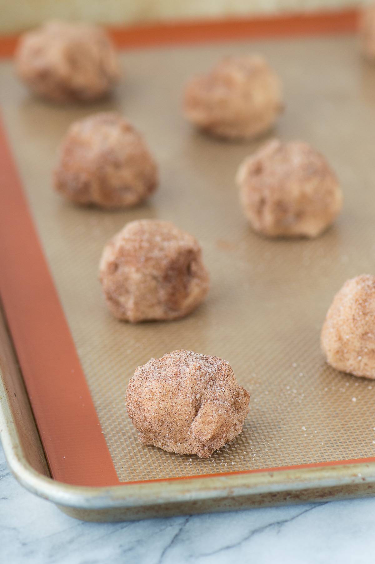 Caramel apple snickerdoodle dough balls lined up on silicone baking mat on metal baking sheet