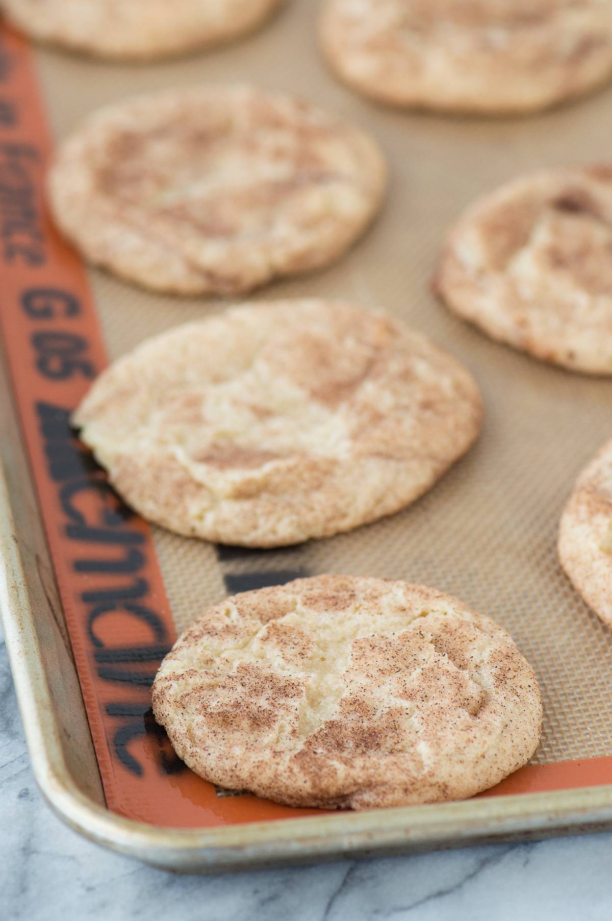 Caramel apple snickerdoodles lined up on silicone baking mat on metal baking sheet