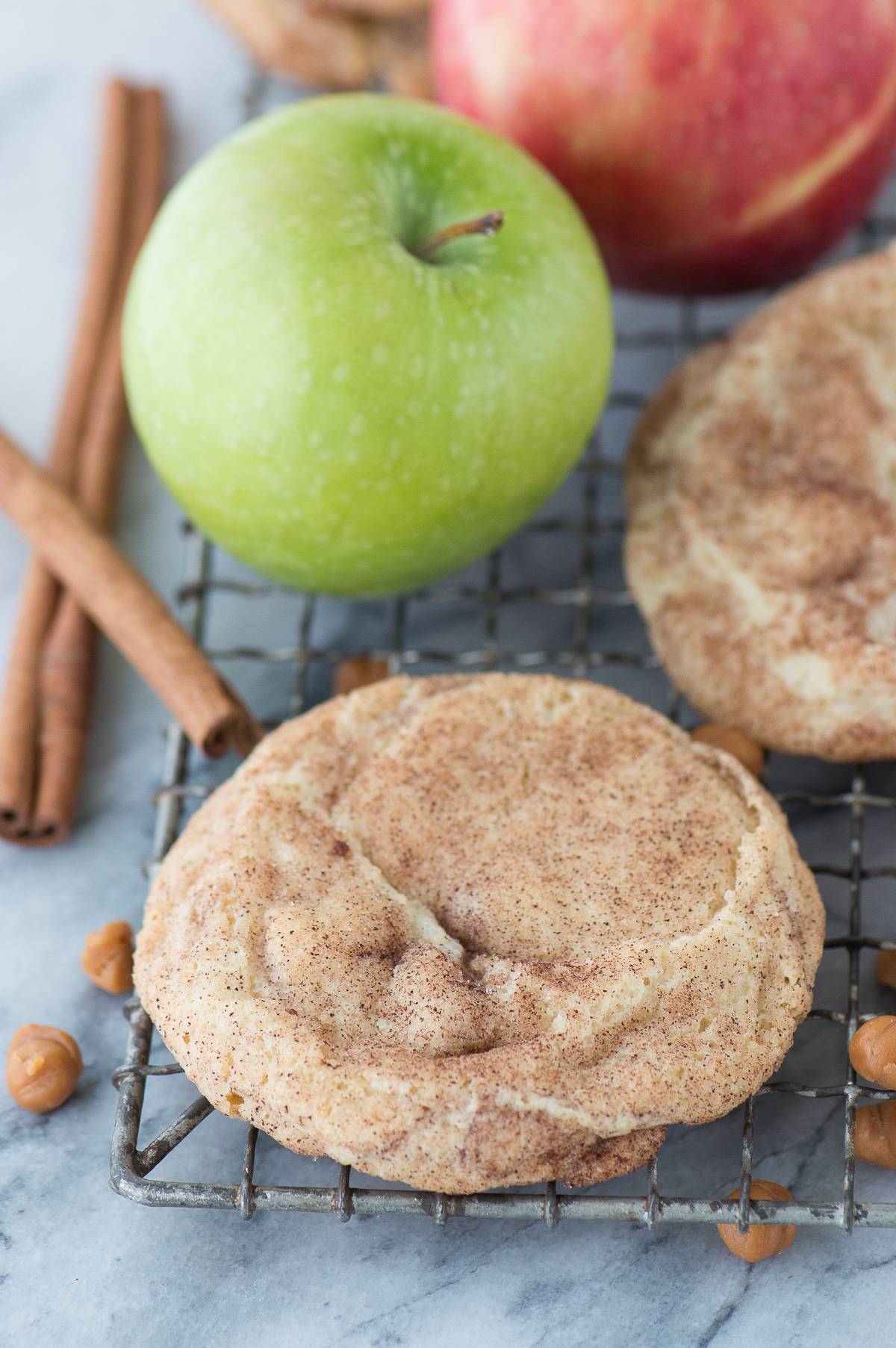 caramel apple cookie on wire cooling rack with caramel bits, cinnamon sticks and apple in the background