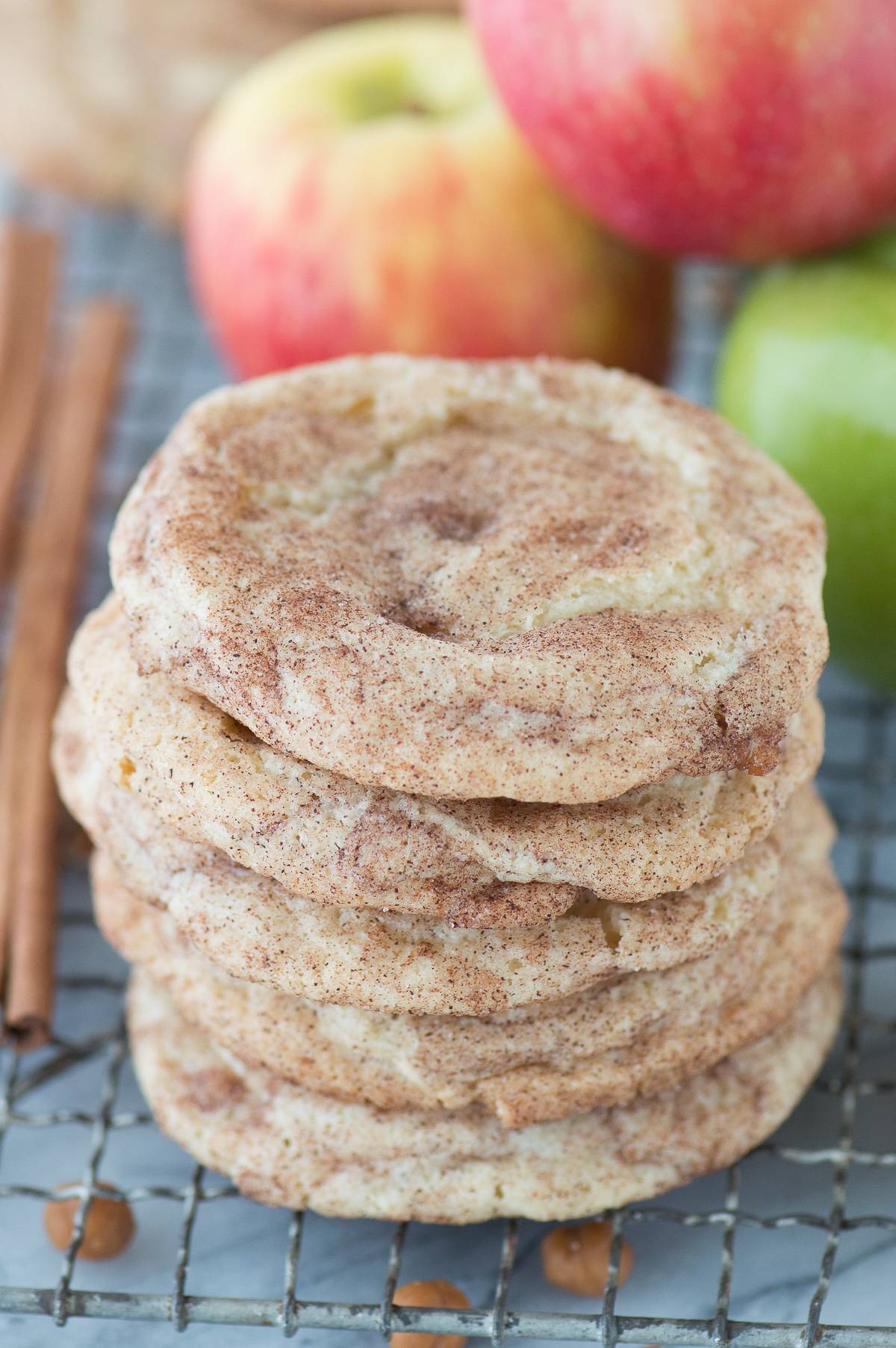 caramel apple snickerdoodle cookies stacked on top of each other on a metal cooking rack with apples in background