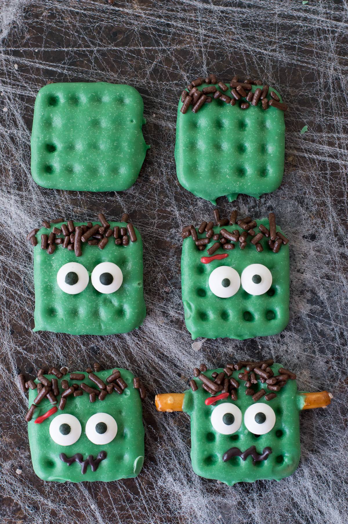 step by step how to make frankenstein treats made out of square waffle pretzels dipped in green chocolate with decorative embellishments on dark background