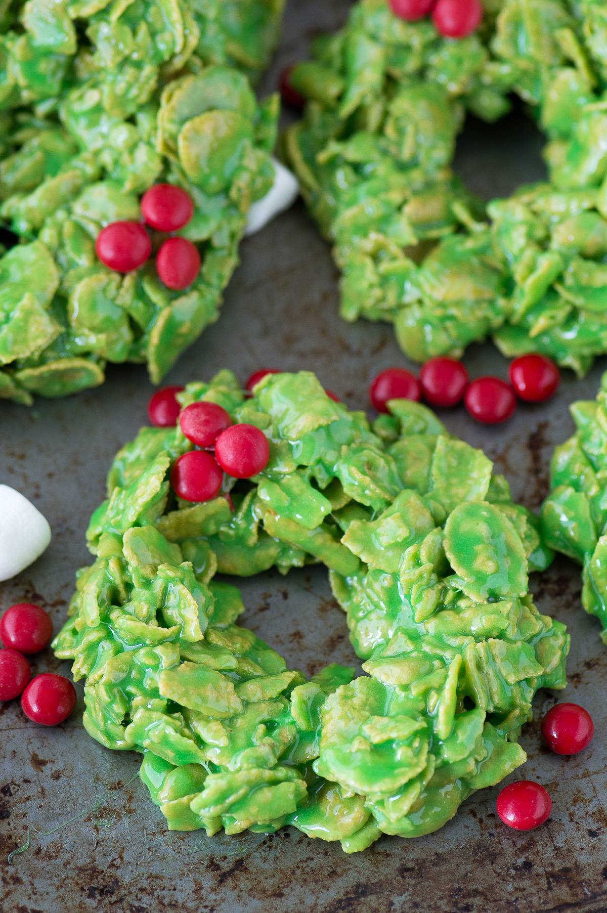 green christmas wreath cookies made with corn flakes and red mms on metal surface