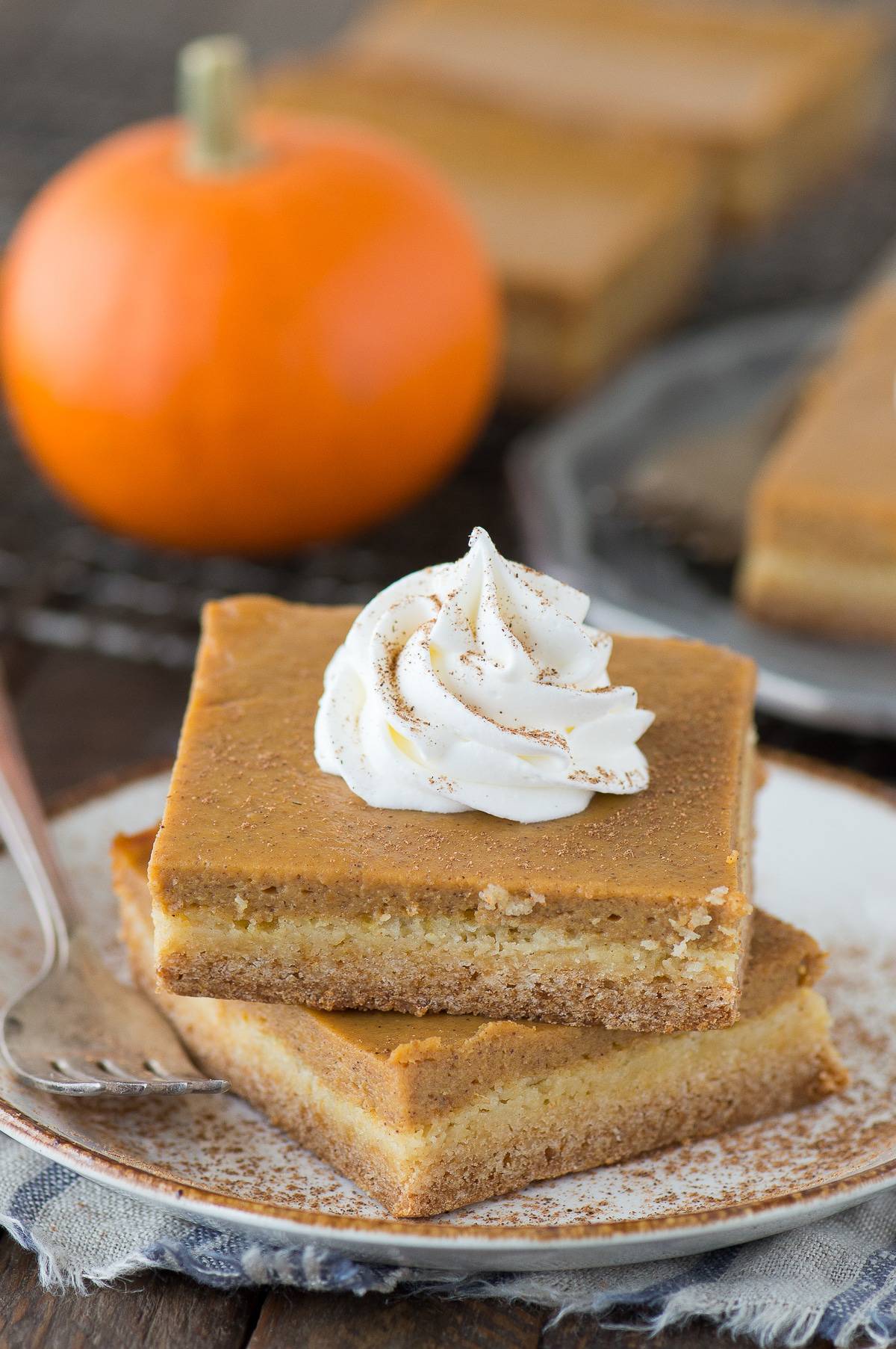 2 pumpkin pie bars stacked on top of each other on white plate with dollop of whipped cream on top