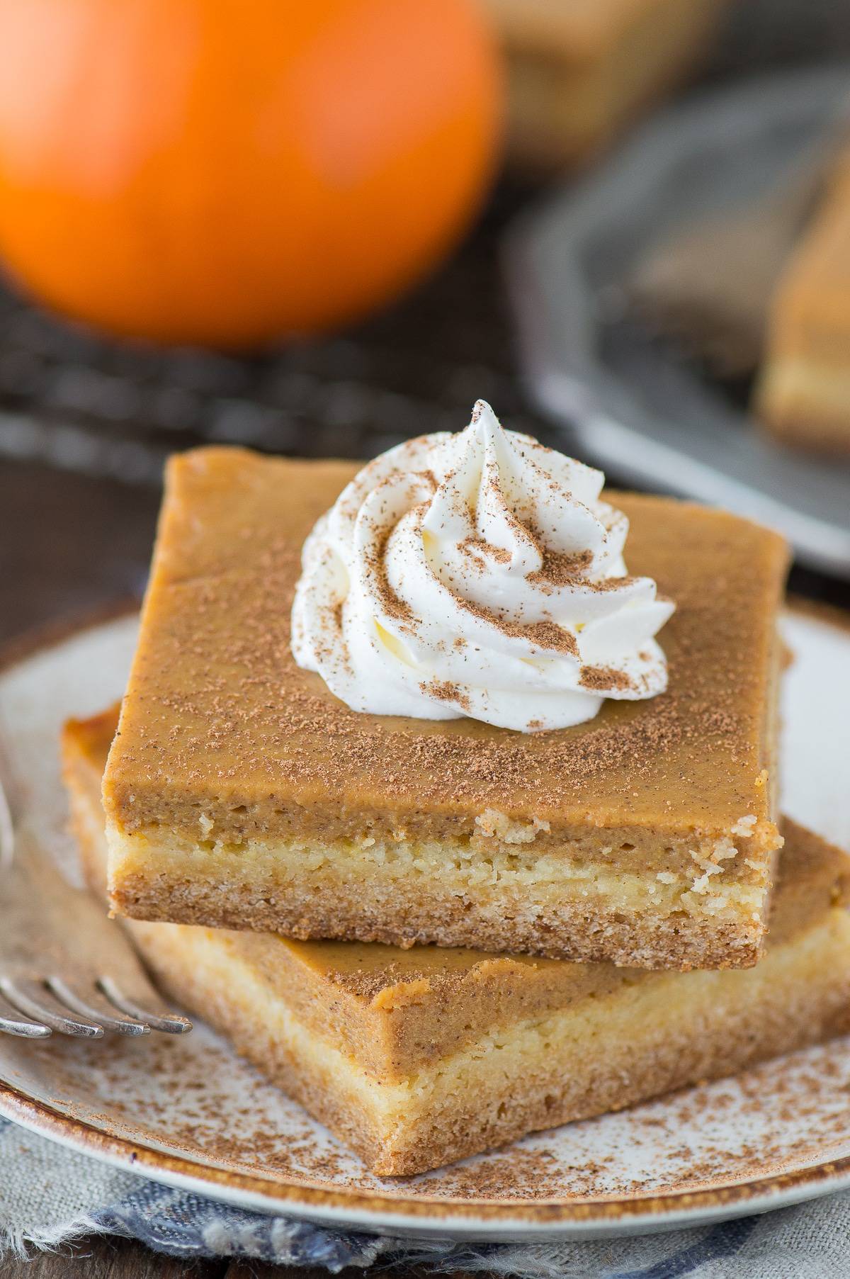 2 pumpkin pie bars stacked on top of each other on white plate with dollop of whipped cream on top