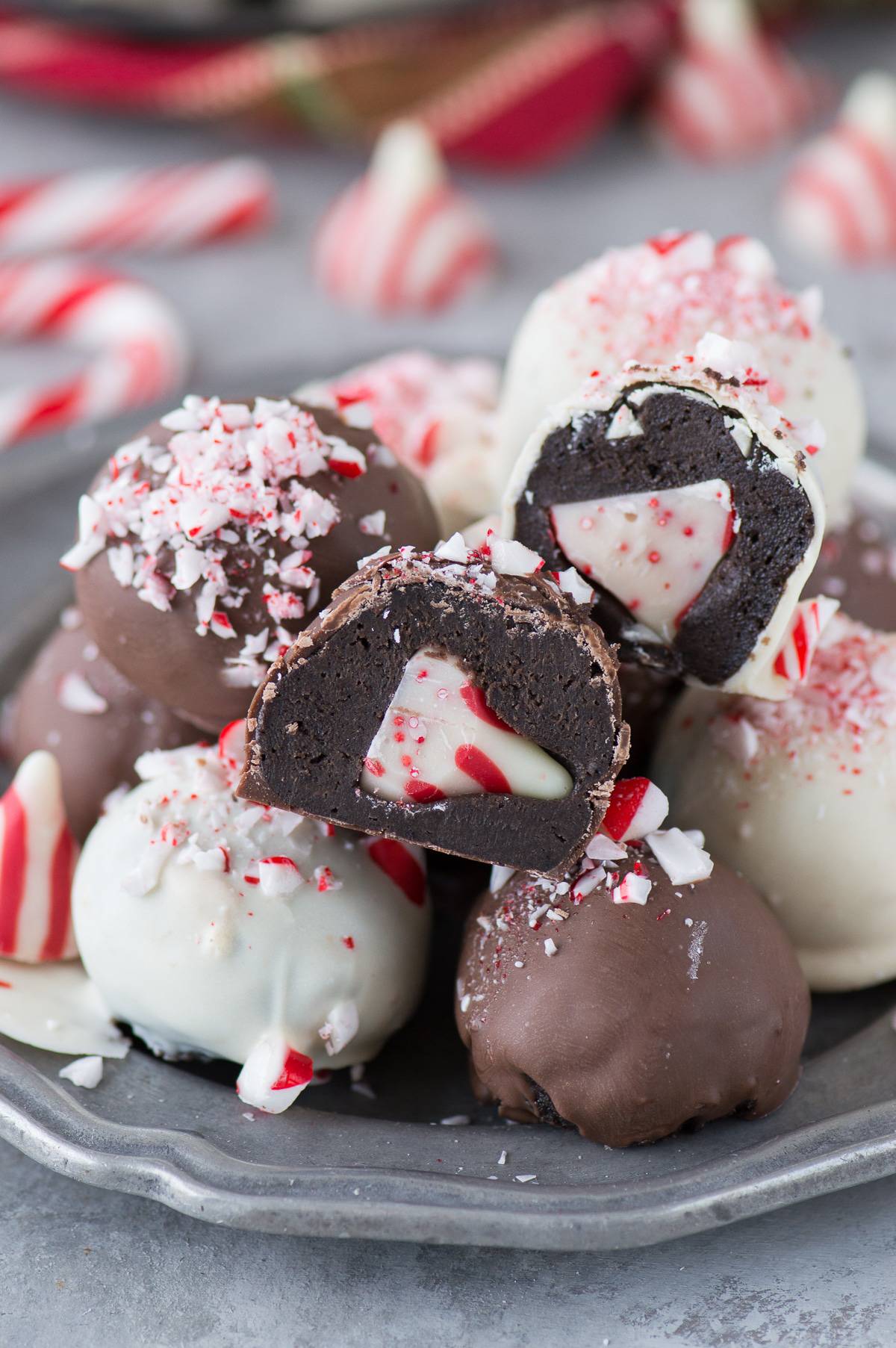 chocolate and white chocolate peppermint oreo balls on metal plate. Two oreo balls are cut open to show the peppermint hershey kiss inside the oreo ball.