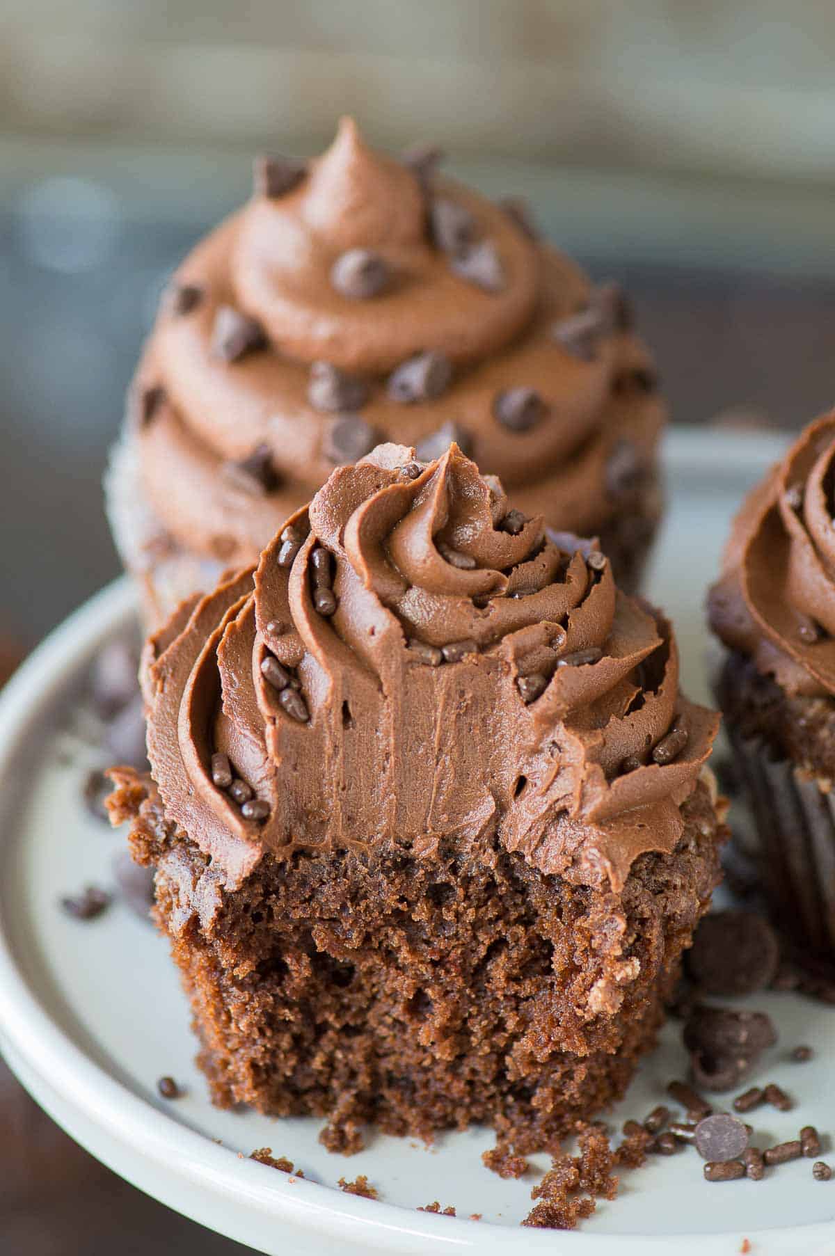 chocolate cupcake with chocolate frosting with bite removed on gray cake stand