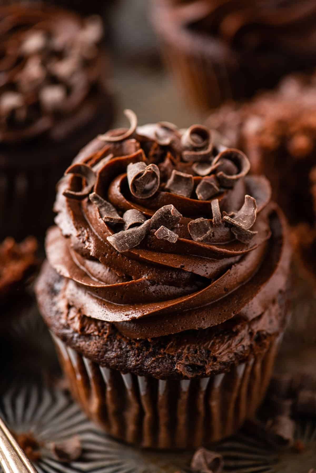 chocolate cupcake with chocolate frosting on metal background with more cupcakes in the distance