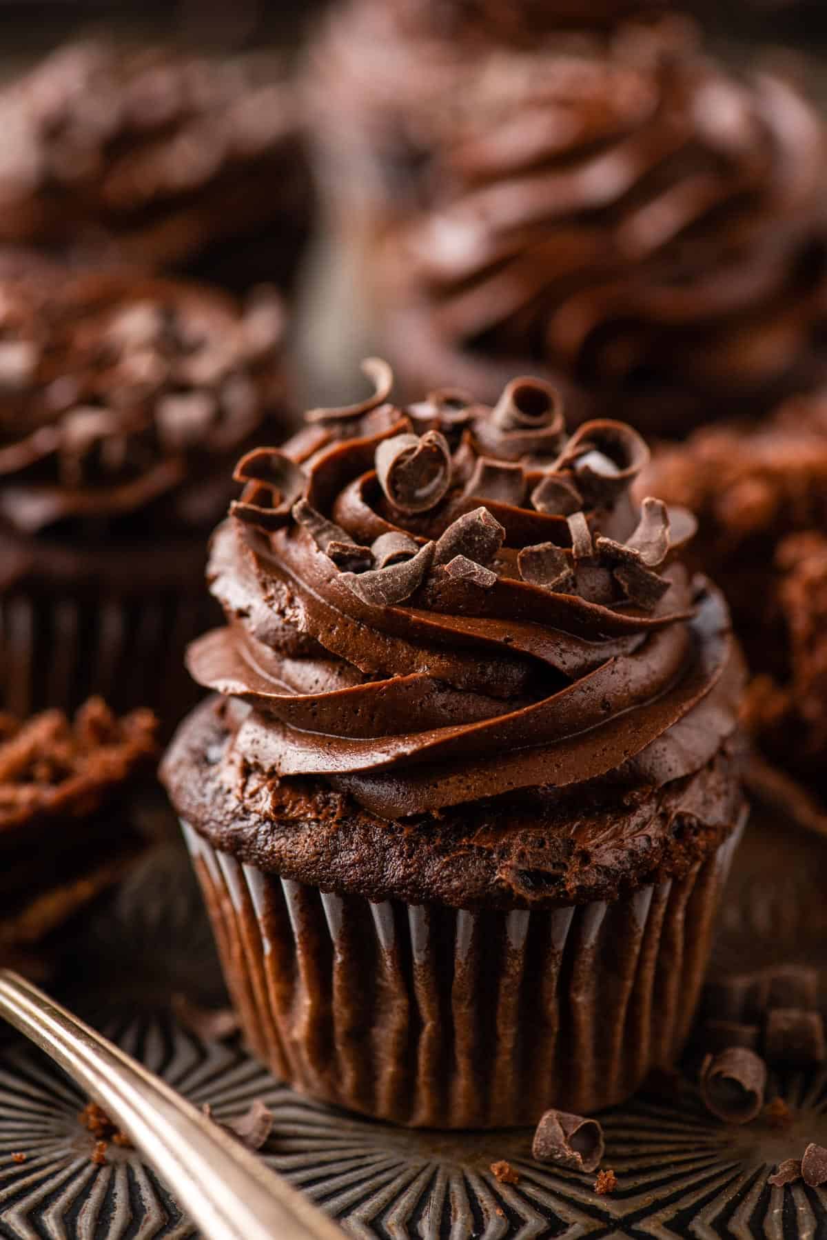 chocolate cupcake with chocolate frosting on metal background with more cupcakes in the distance