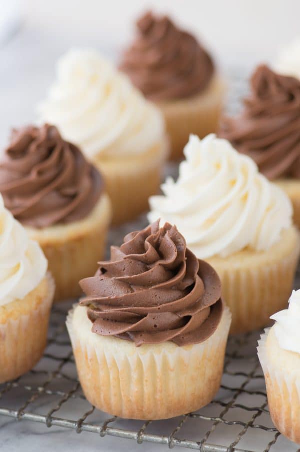 This CLASSIC WHITE CUPCAKE recipe is AMAZING! This is our go-to white cupcake recipe because it’s so moist and flavorful. Pair these cupcakes with vanilla or chocolate frosting. This is our go to moist white cupcake recipe to make for a wedding, baby shower, or any party. white cupcakes with vanilla and chocolate frosting on wire cooling tray