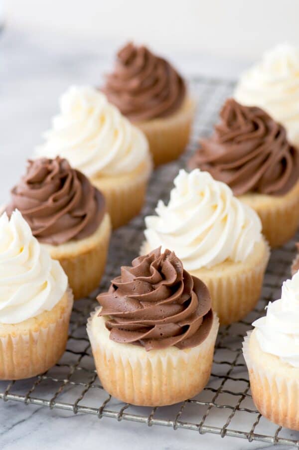 vanilla cupcakes with chocolate and white frosting on metal cooling rack on marble background