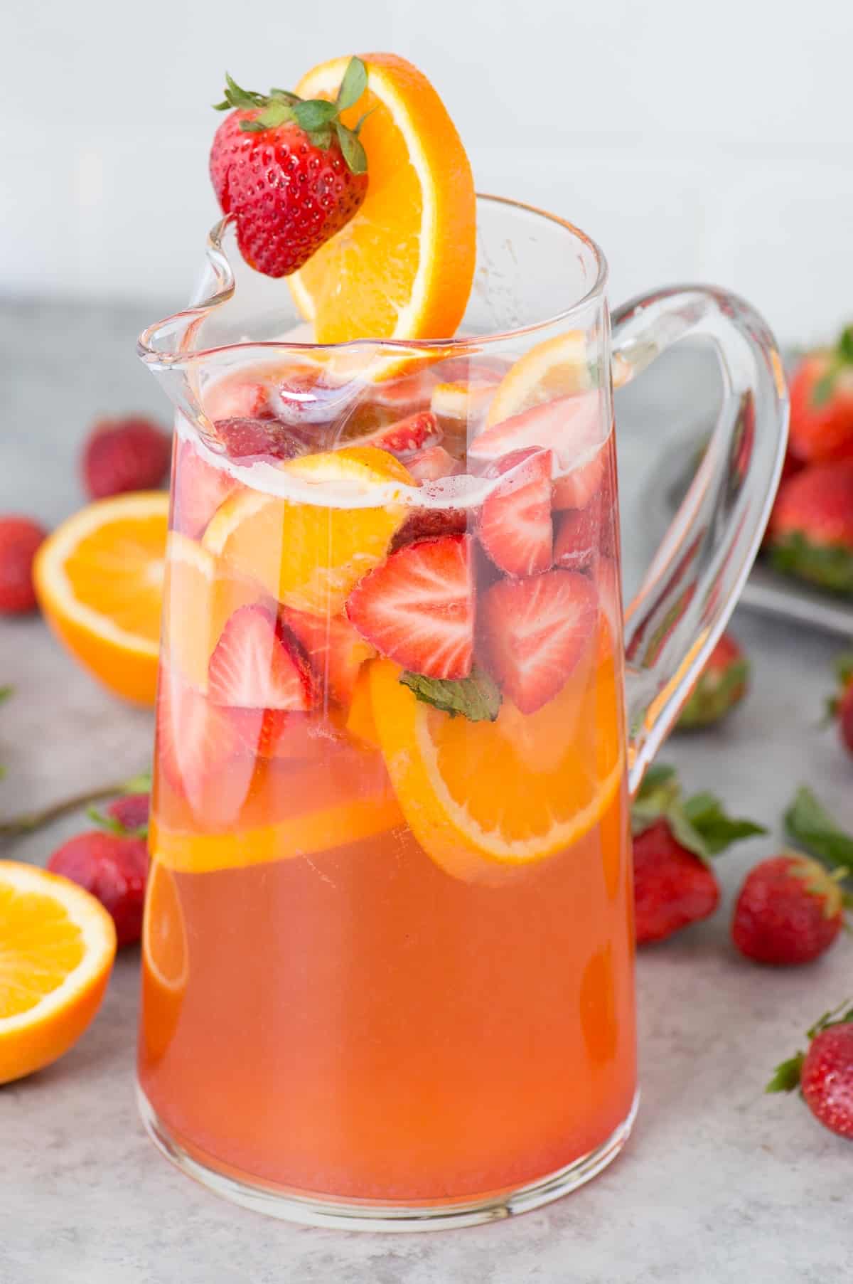 strawberry sangria in glass pitcher with strawberries, oranges and mint as garnish