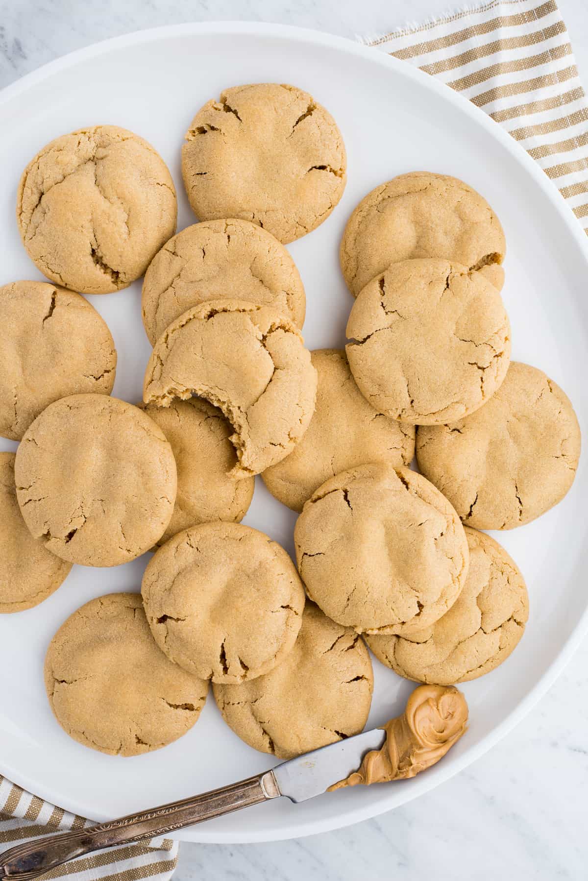 peanut butter cookies on white plate with butter knife with peanut butter on white background