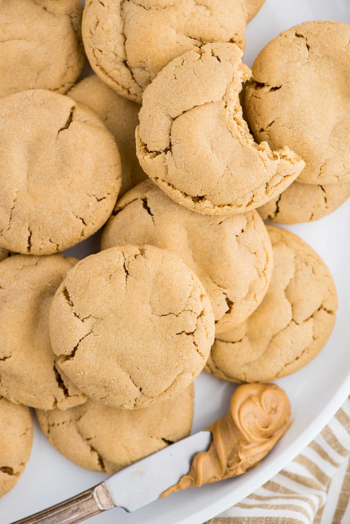 peanut butter cookies on white plate with butter knife with peanut butter on white background