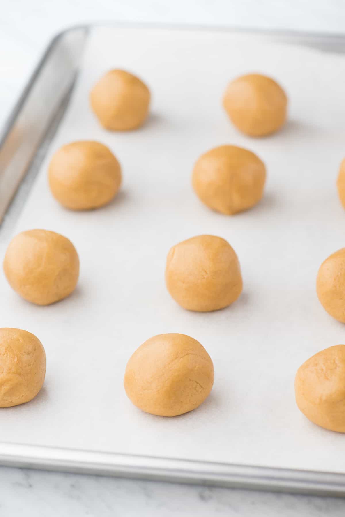 peanut butter cookie dough balls on white parchment paper on baking sheet