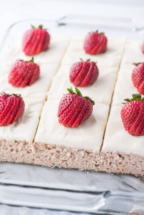 strawberry cake in glass pan with white frosting and a strawberry on each piece