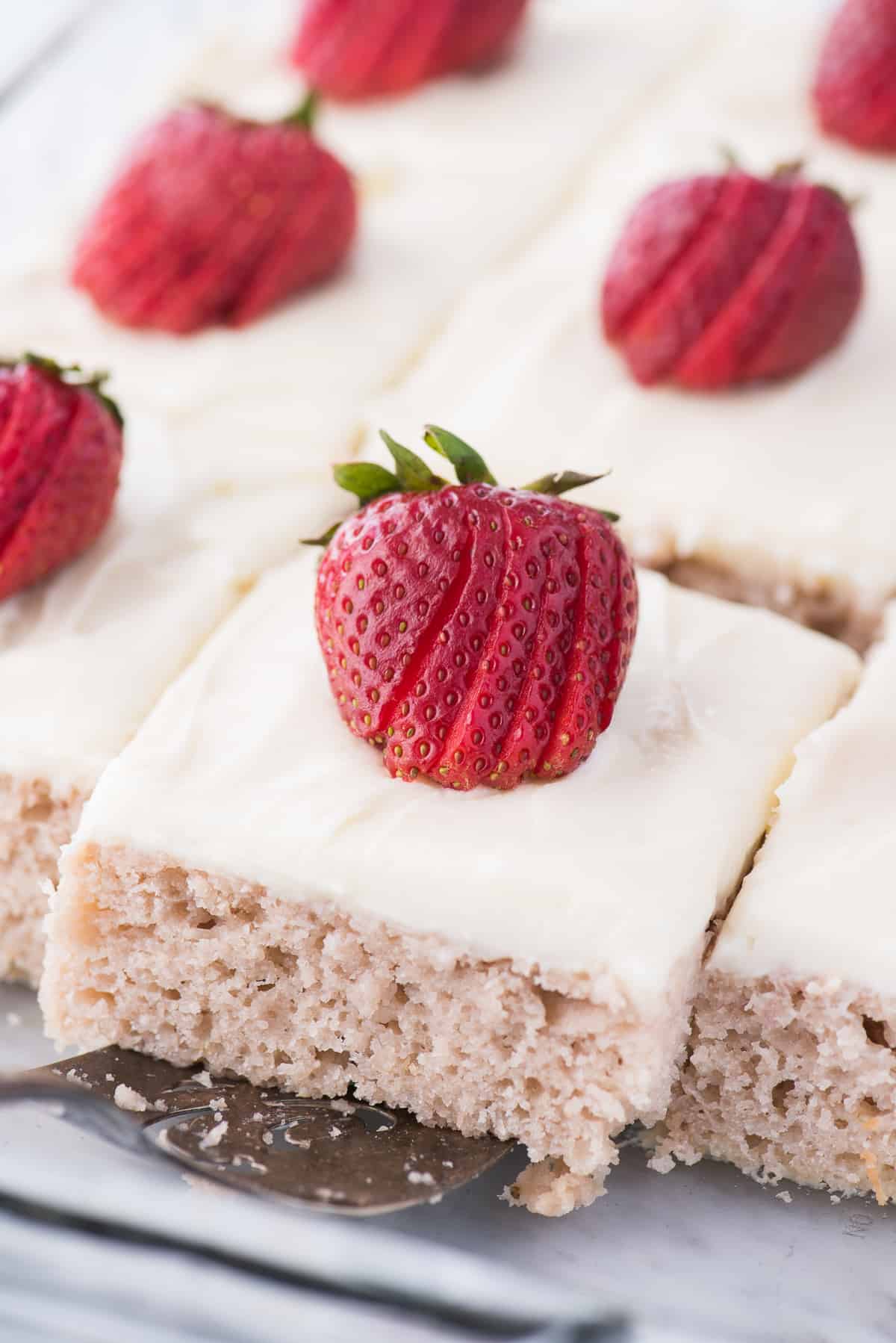 strawberry cake with white frosting and strawberry on top on metal spatula