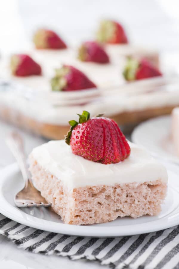 strawberry cake with white frosting and strawberry on top on white plate