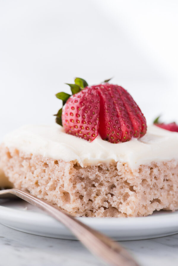 strawberry cake with cream cheese frosting on white plate with bite removed