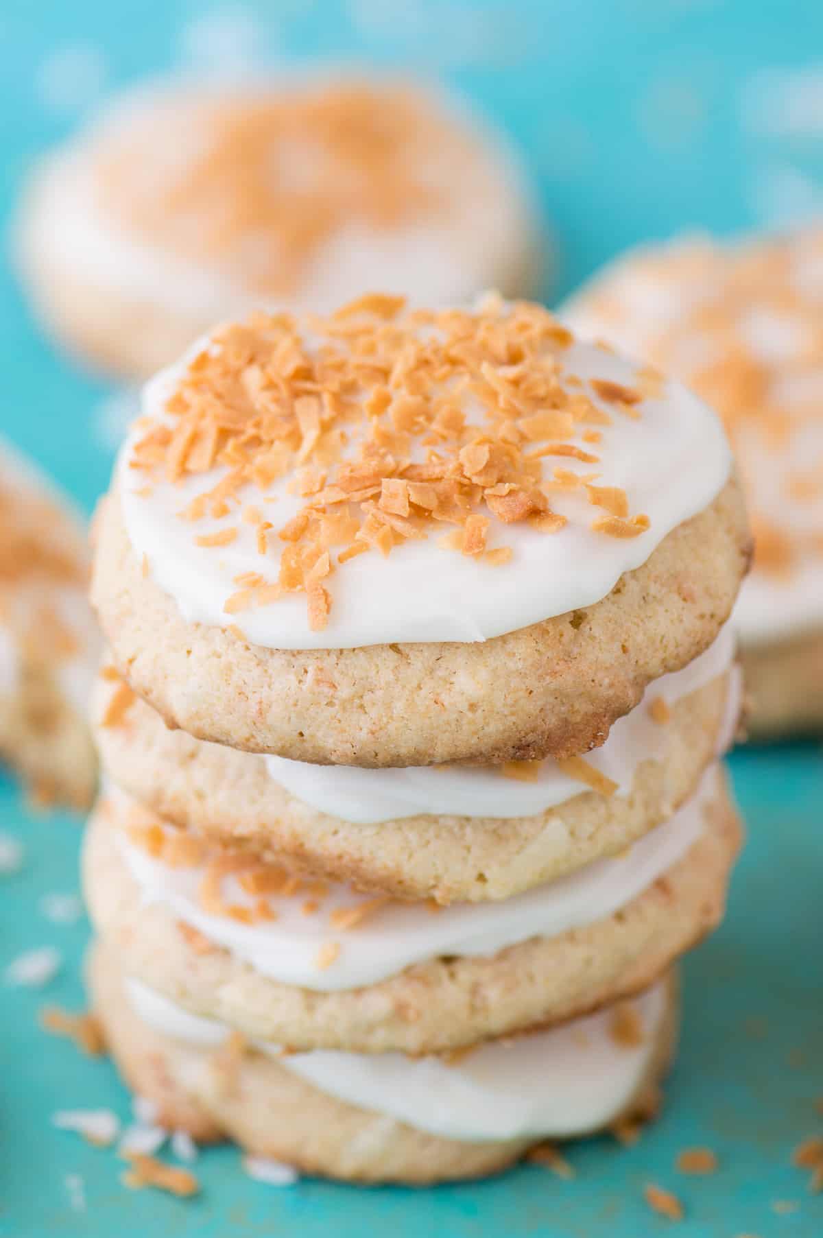 coconut cookies with white frosting in a stack on a teal background