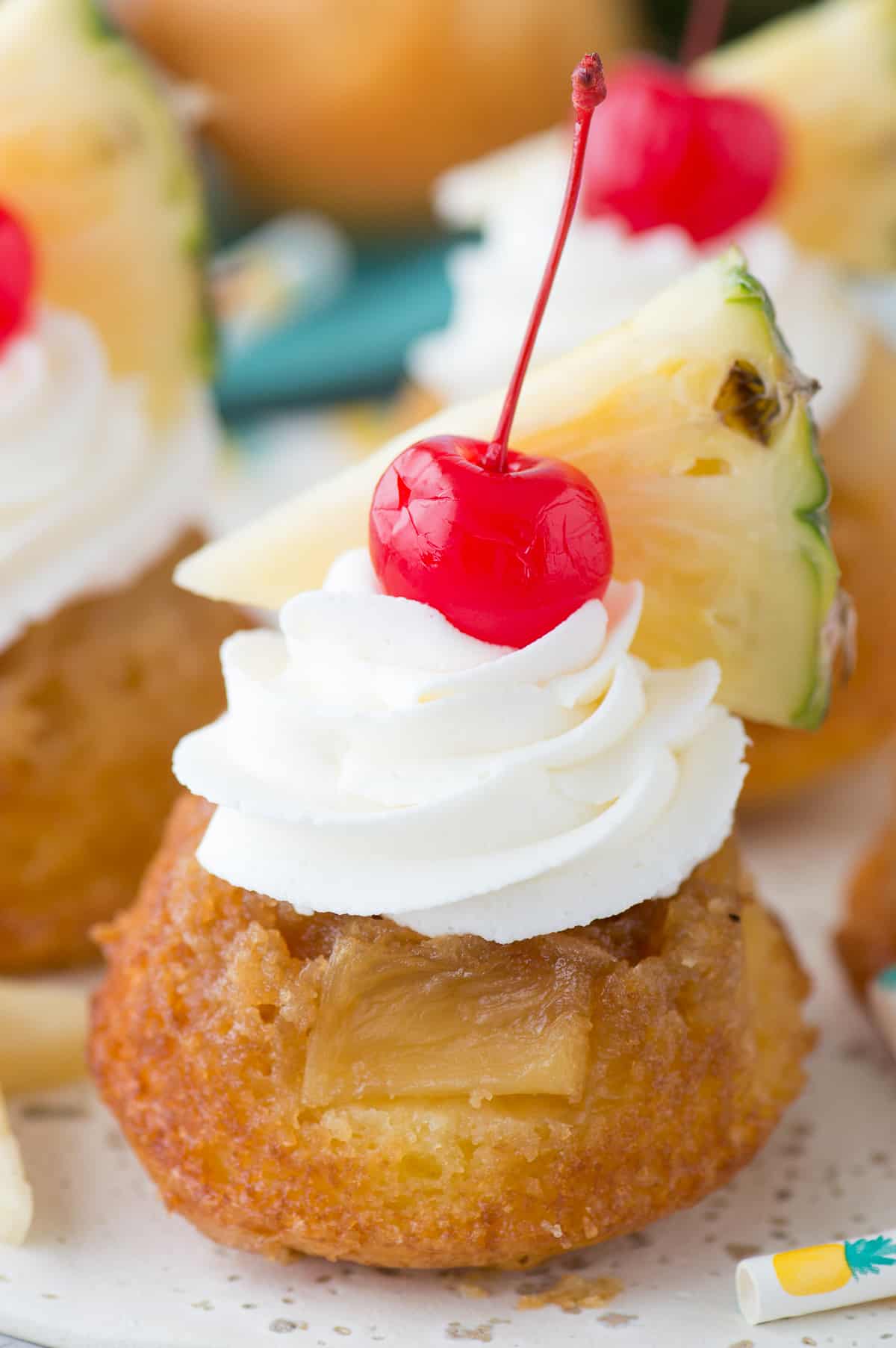 mini pineapple upside down cakes with whipped cream, a cherry and pineapple slice on white plate