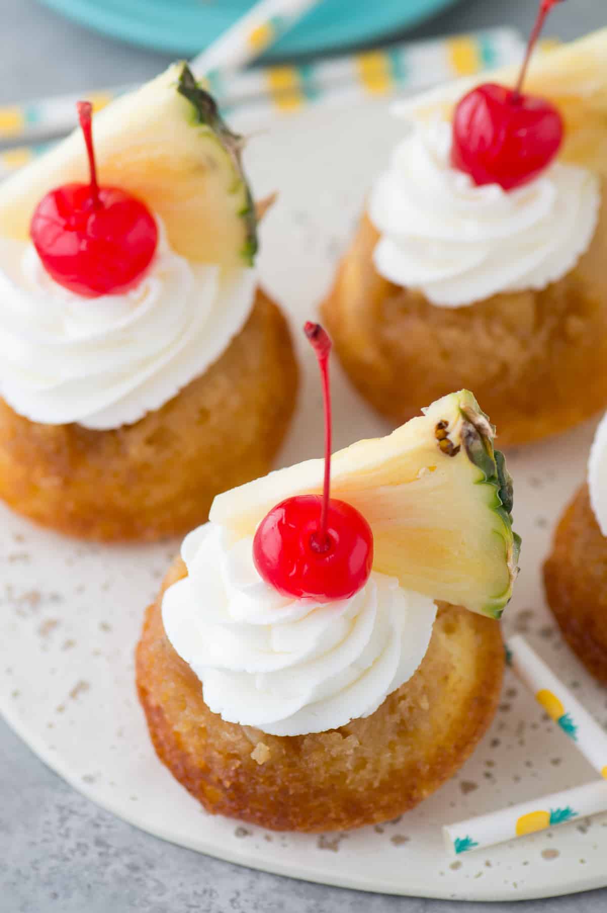 mini pineapple upside down cakes with whipped cream, a cherry and pineapple slice on white plate