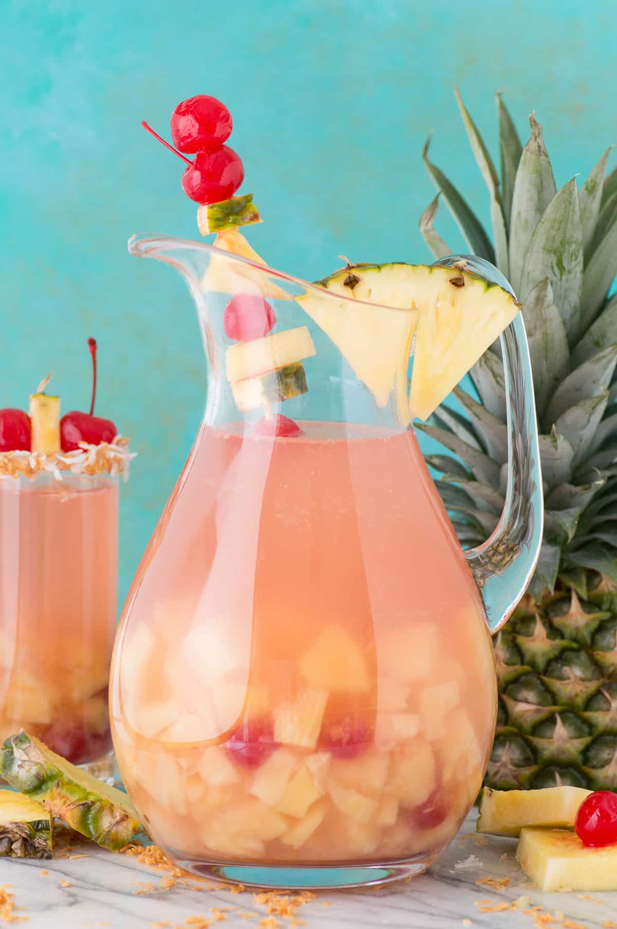 pina colada sangria in a glass pitcher with pineapple and cherry for garish