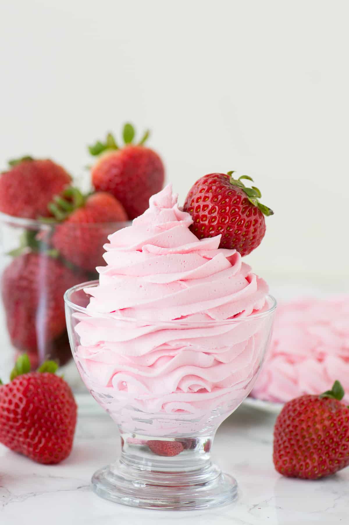 strawberry whipped cream piped into clear glass with strawberries in the background