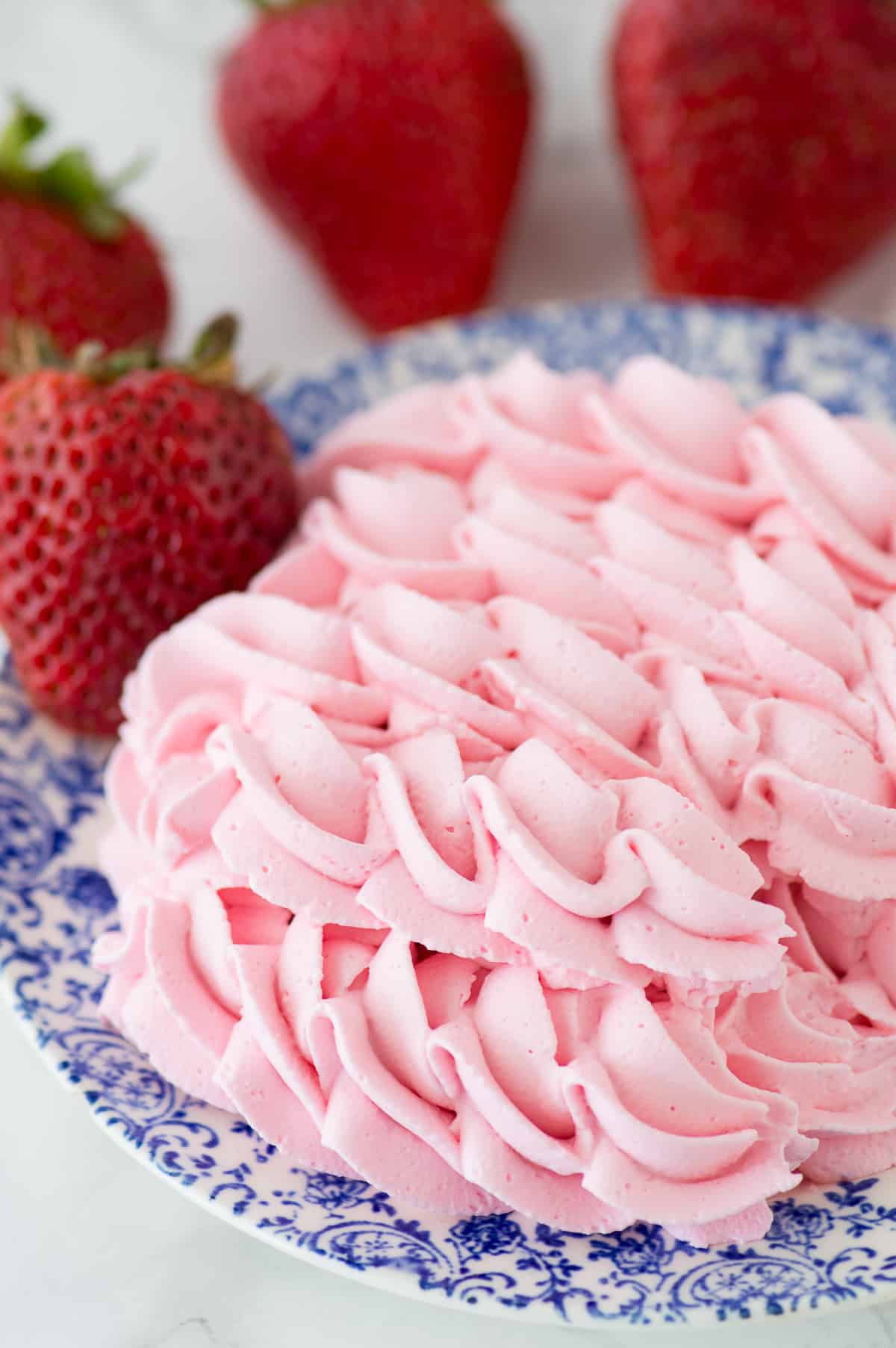 strawberry whipped cream piped onto blue floral plate with strawberries in the background