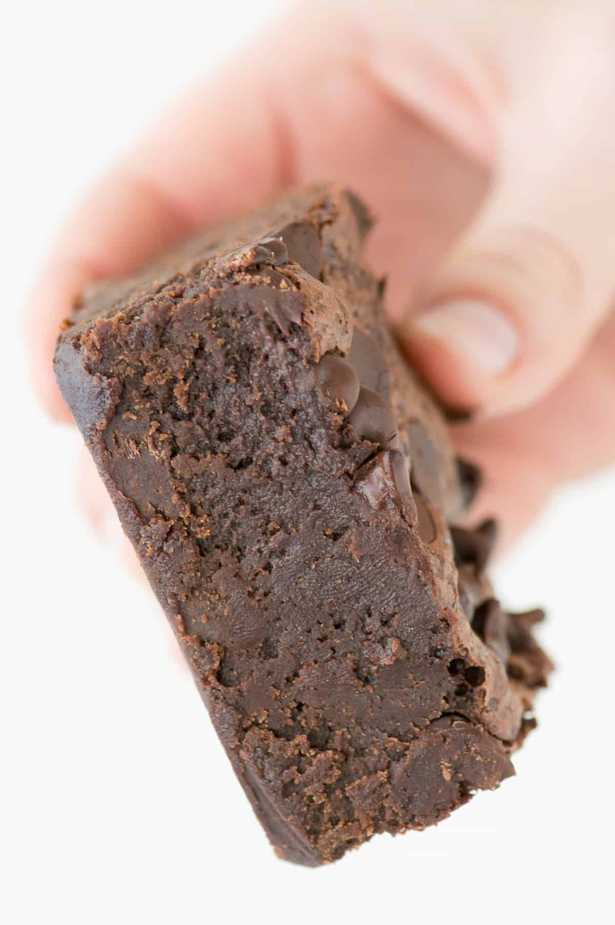 hand holding one fudgy brownie on white background
