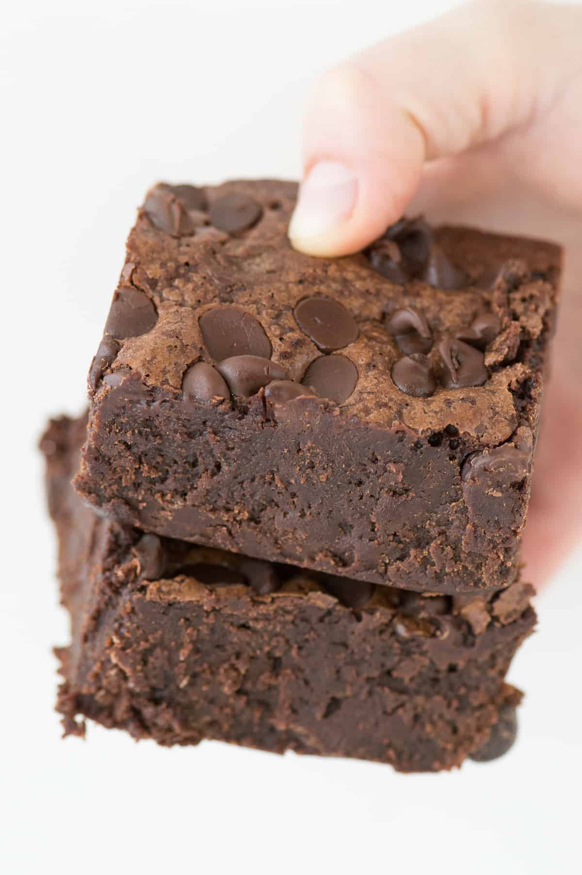 hand holding two fudgy brownies on white background