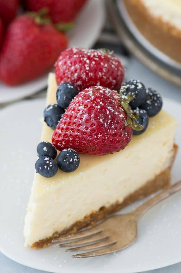 slice of classic plain cheesecake with fruit on top on white plate