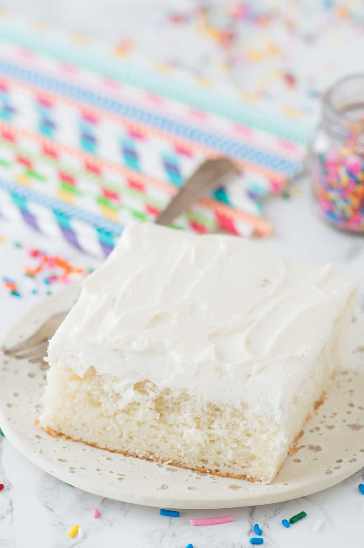 slice of white cake on white plate with colorful straws in background