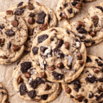A close-up of several cookies and cream cookies, topped with chunks of chocolate sandwich cookies, arranged on brown parchment paper—perfect for any Oreo cookies recipe lover.