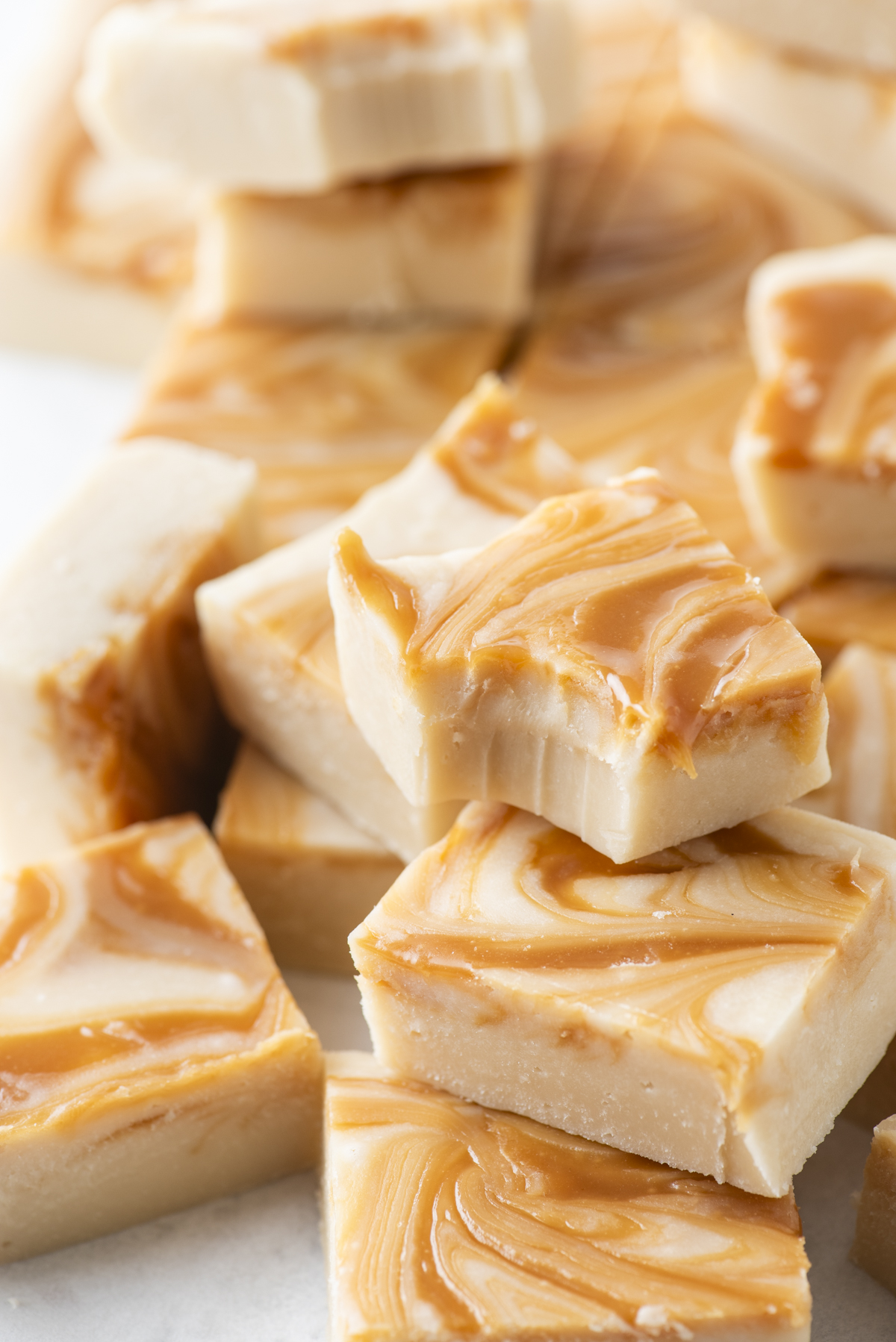 Squares of creamy white fudge with golden caramel apple fudge swirls stacked on top of each other, showing a smooth, rich texture and a glossy finish.