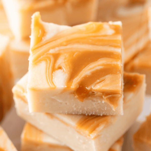 Close-up of creamy caramel apple fudge squares stacked, showcasing a smooth texture and rich caramel swirls on top.